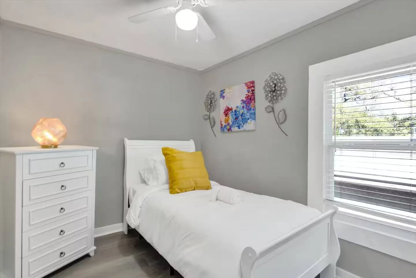 Bedroom featuring a white twin bed, white dresser with a salt lamp, gray walls, ceiling fan, and a window with blinds.