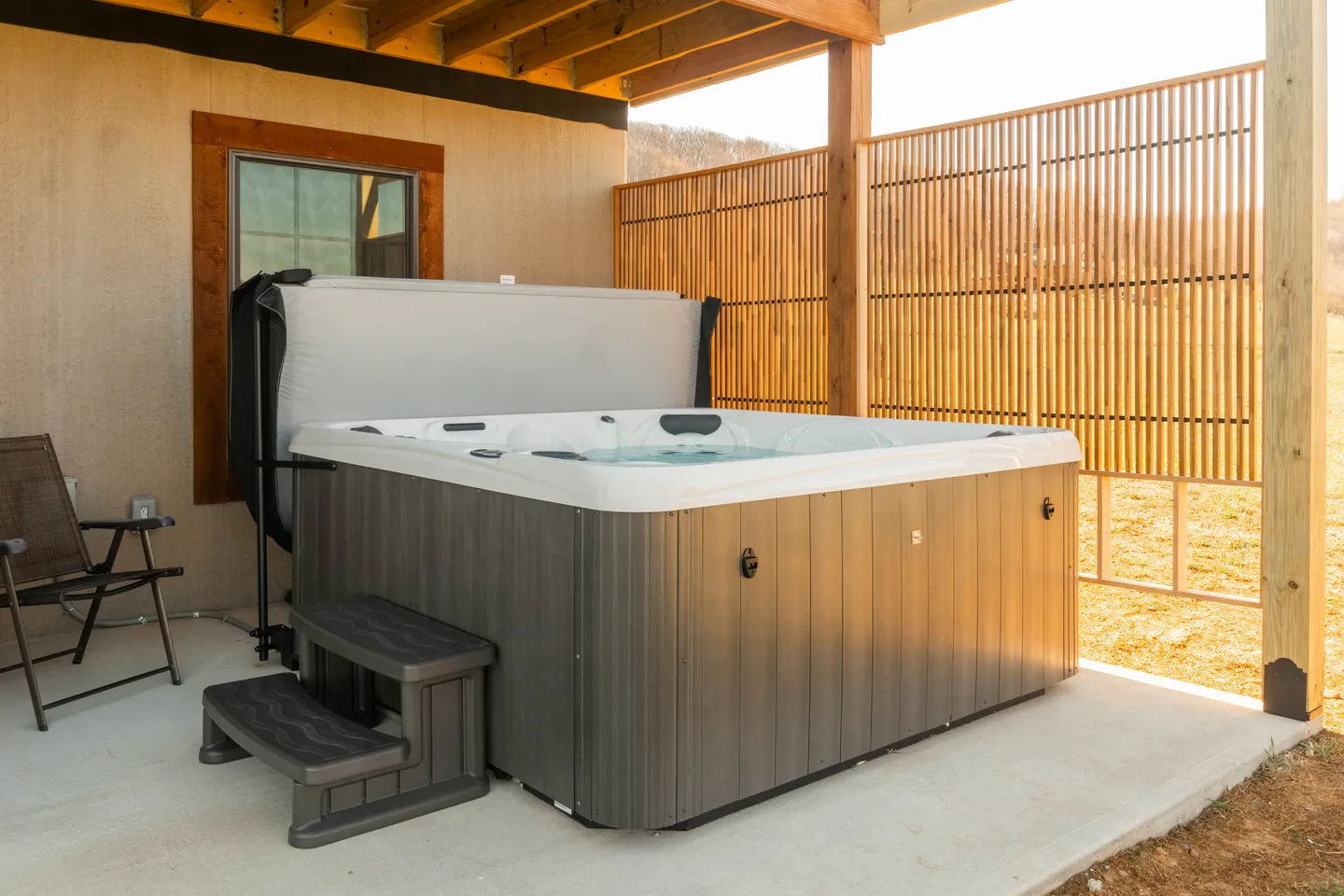 Outdoor hot tub filled with water on a concrete patio beside a wooden slat privacy screen.