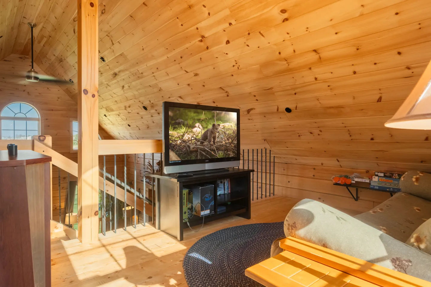Upstairs wood-paneled loft area with a television on a stand, a ceiling fan, and seating under a sloped ceiling.