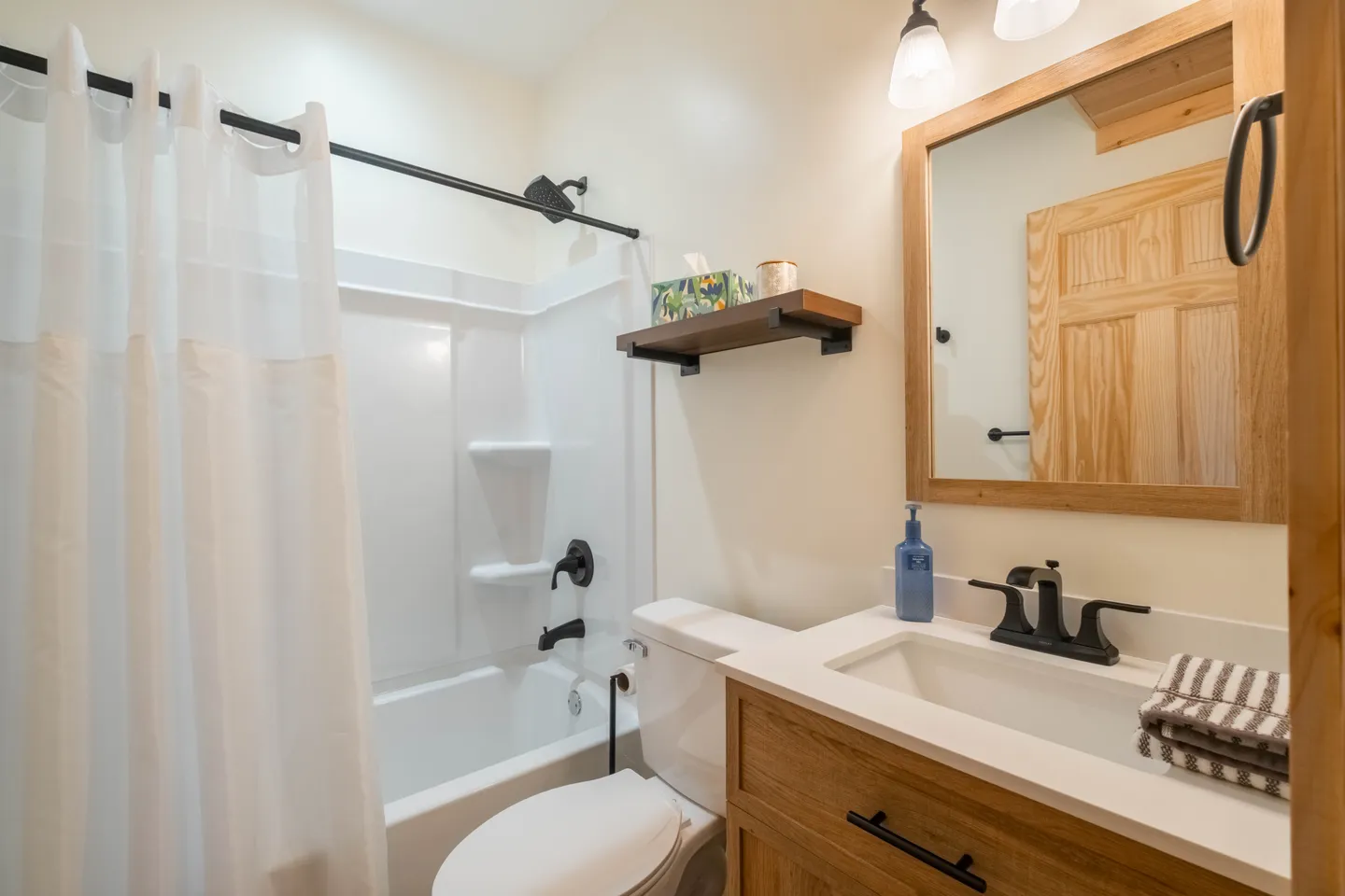 Bathroom with a wood vanity, white countertop, framed mirror, toilet, and combination bathtub and shower with a white curtain.