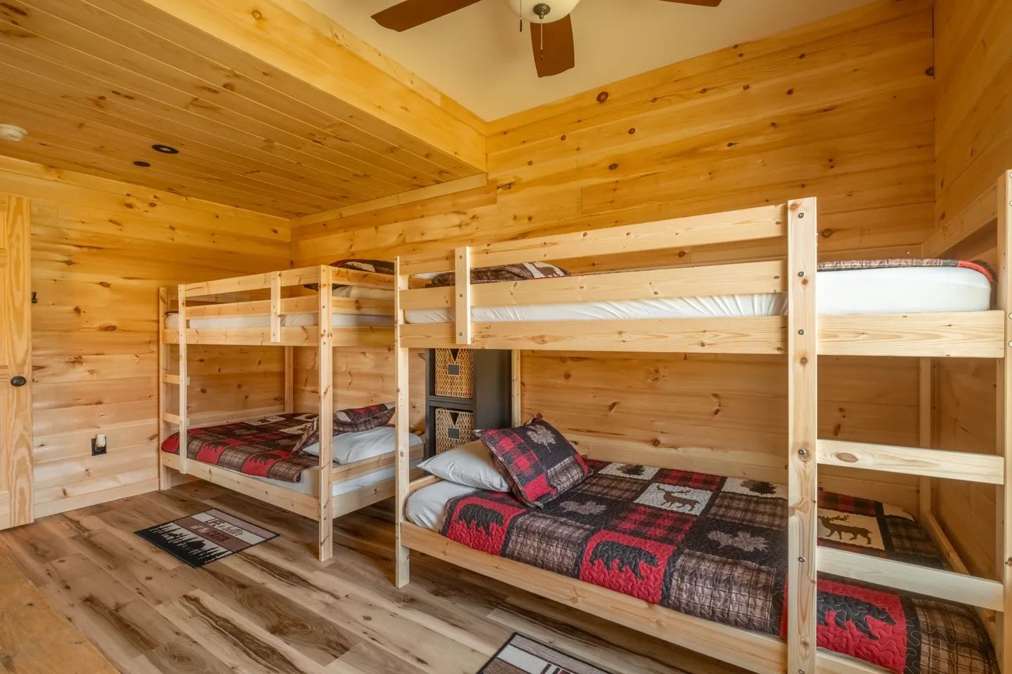 Bedroom with all-wood paneling, ceiling fan, and two sets of wooden bunk beds dressed in rustic wildlife-themed bedding.