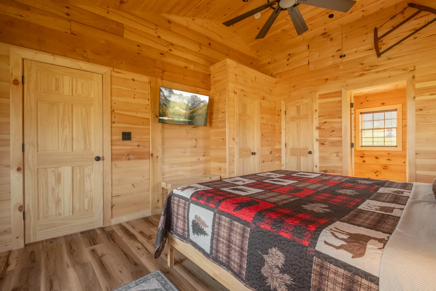 Bedroom with all-wood plank walls and ceiling, featuring a bed with a rustic patchwork quilt and a wall-mounted TV.