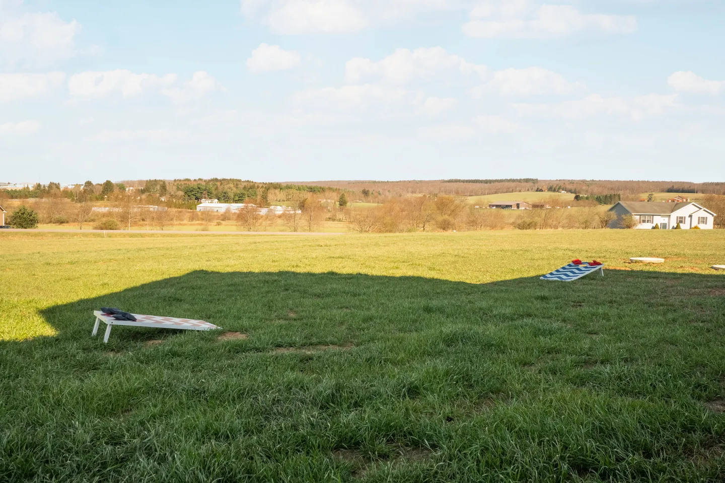 Open grassy lawn with cornhole boards set up under a partly cloudy sky with distant countryside views.
