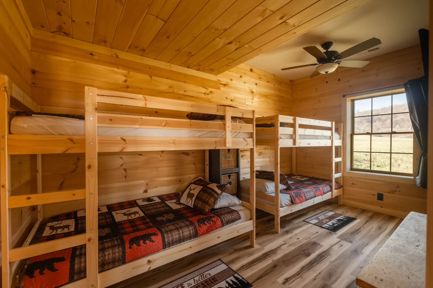 A wood-paneled bunk bedroom with two wooden bunk beds, patterned bedding, and a window.