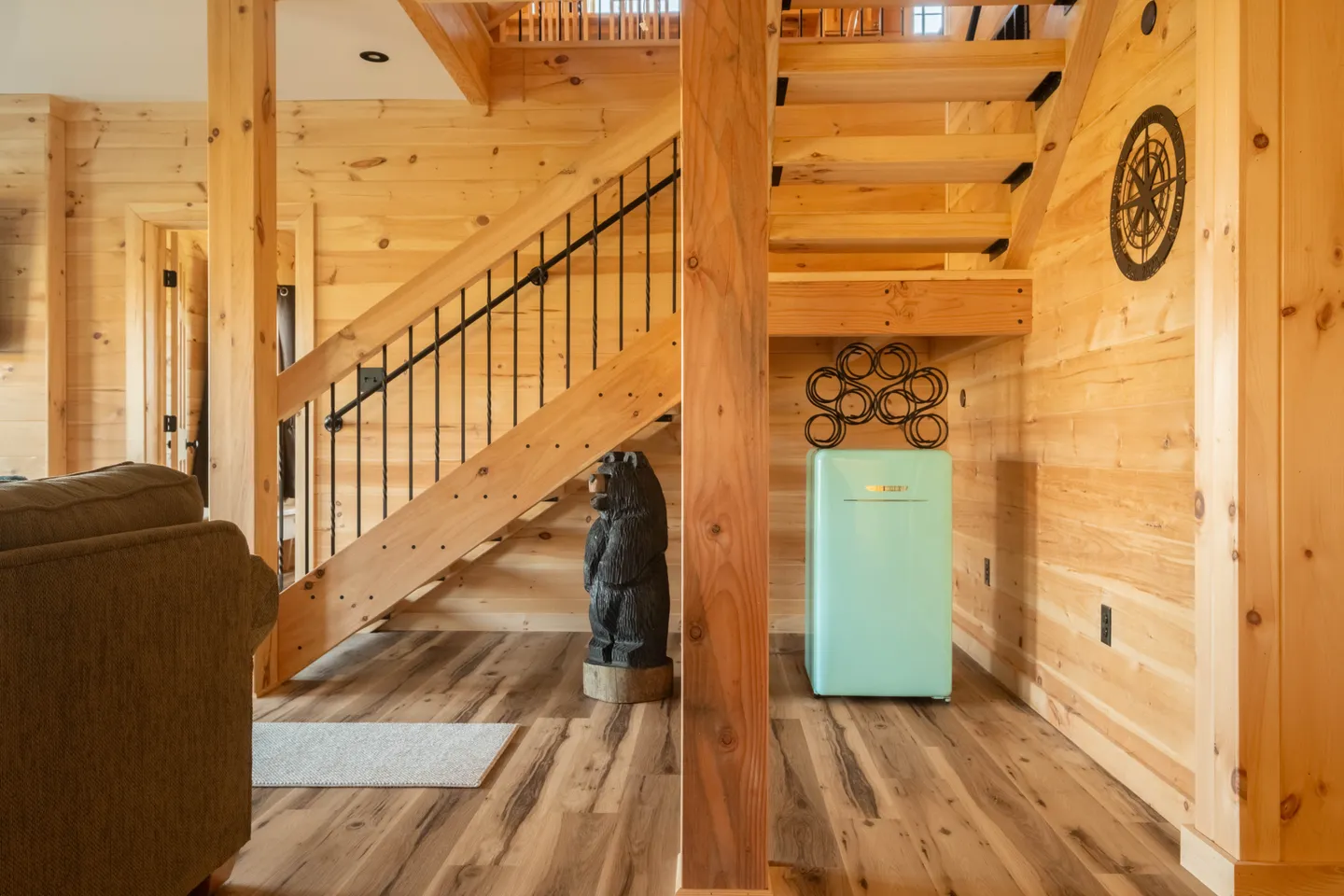 Open wooden staircase in a log cabin style interior with a carved bear statue and mini-fridge underneath.