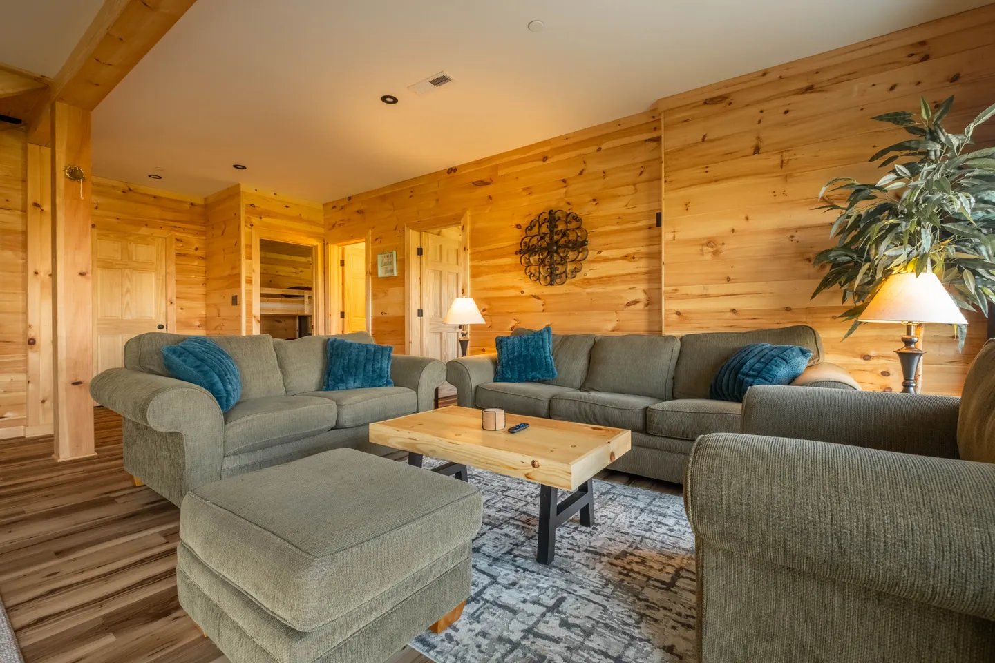 Living room with knotty wood-paneled walls, upholstered seating, and a central coffee table on an area rug.