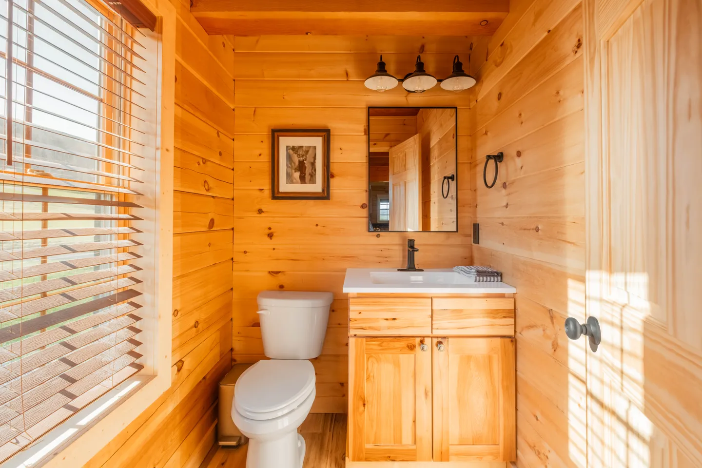 Bathroom with wood-paneled walls, a white toilet, and a wood vanity with a white countertop and black faucet.