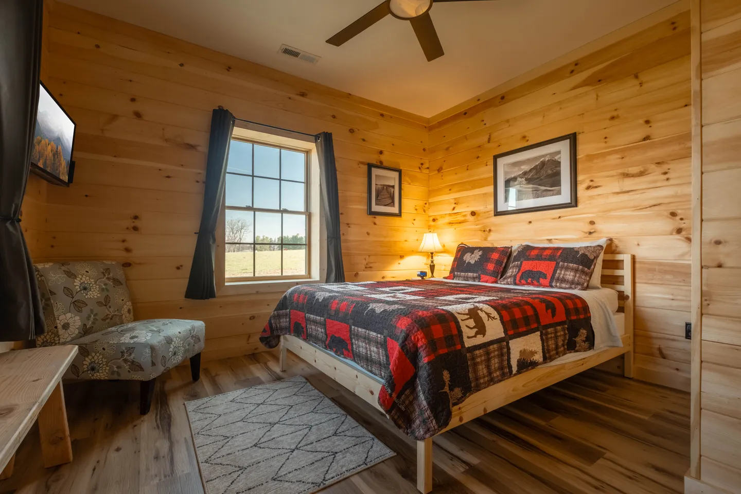 Bedroom with light knotty pine wood walls, wood bed frame, plaid patterned bedding, an armchair, and a window.