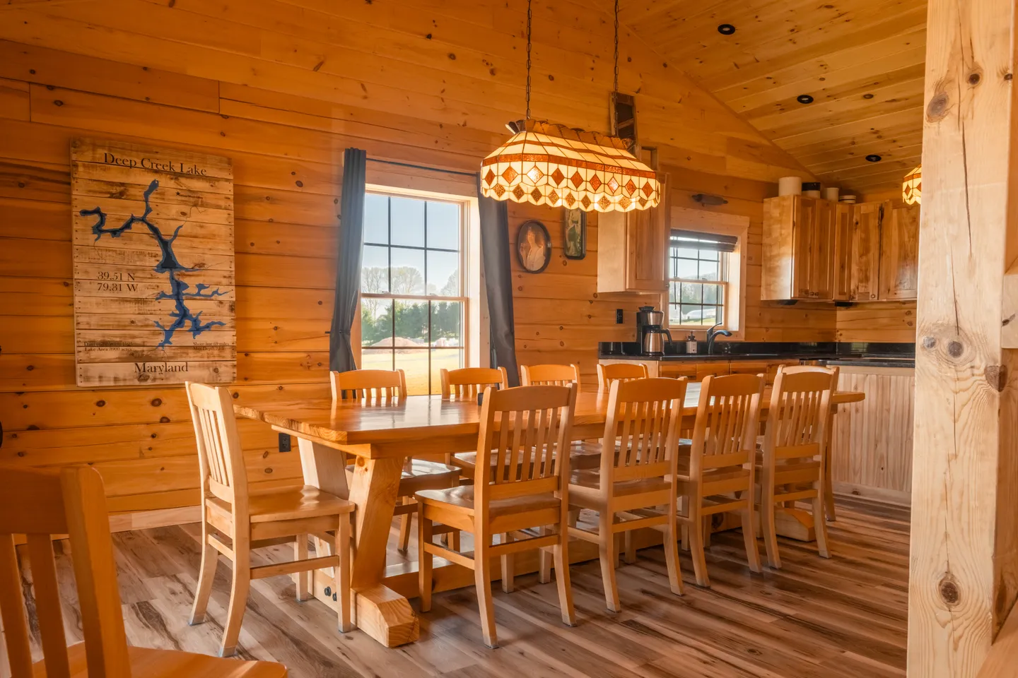 Dining area with a large wooden table and chairs in a cabin-style room with pine wood walls and ceiling.