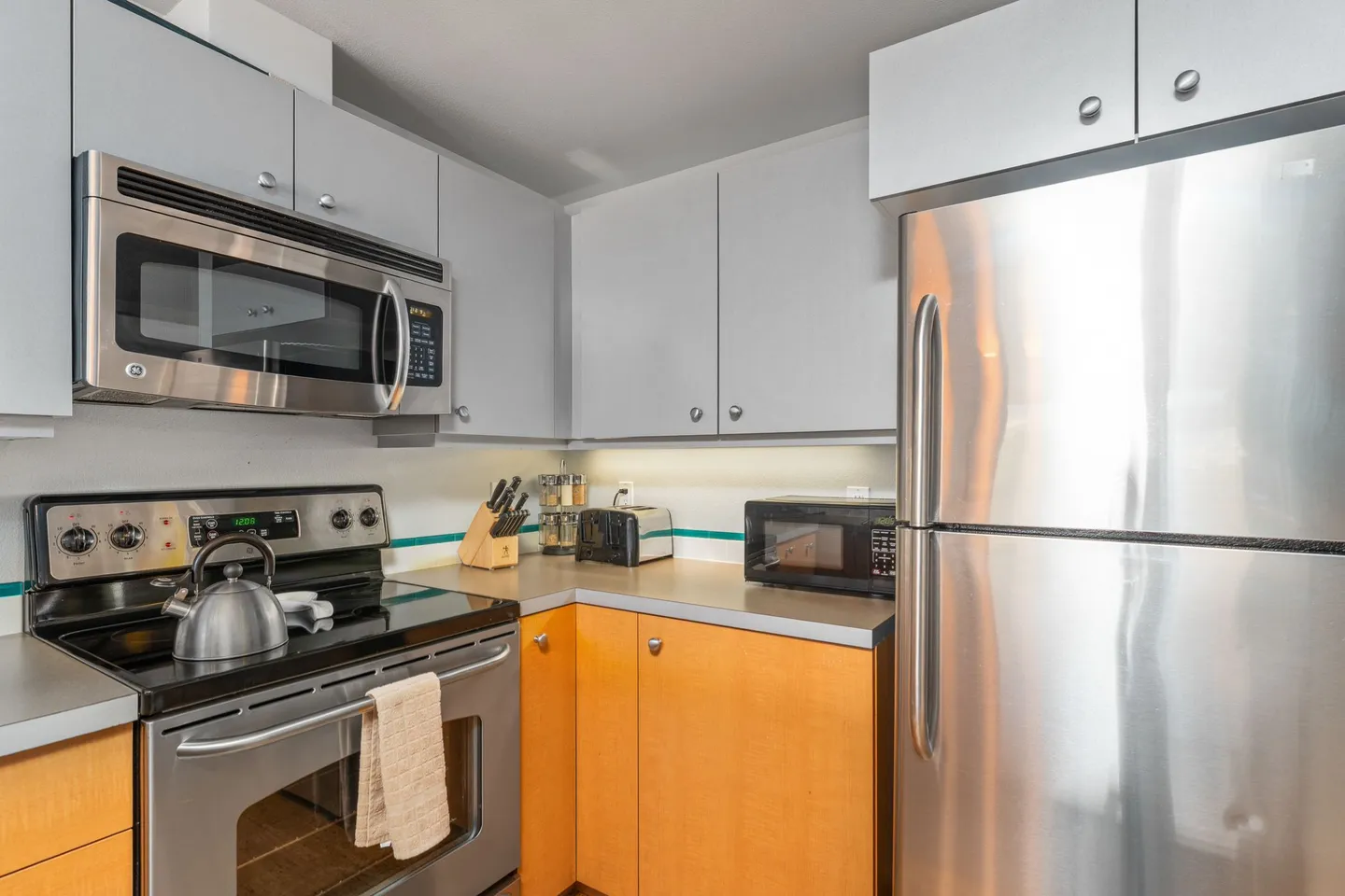 Kitchen corner featuring stainless steel appliances including a refrigerator, stove, oven, microwave, and small appliances on the countertop.