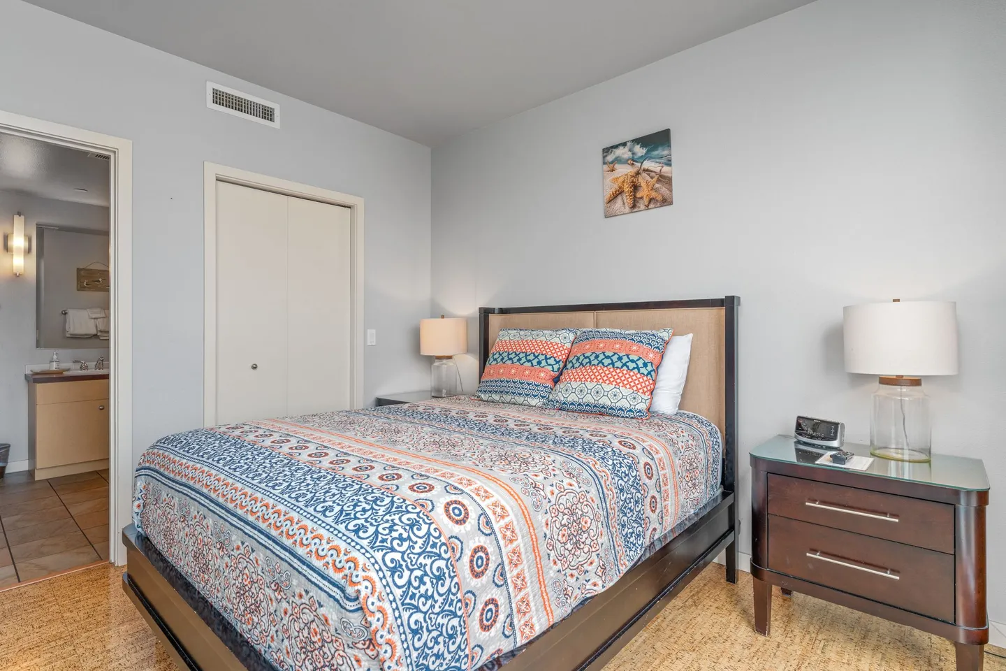 Bedroom with a patterned bedspread, dark wood bed frame, nightstand, and an open doorway leading to a bathroom.