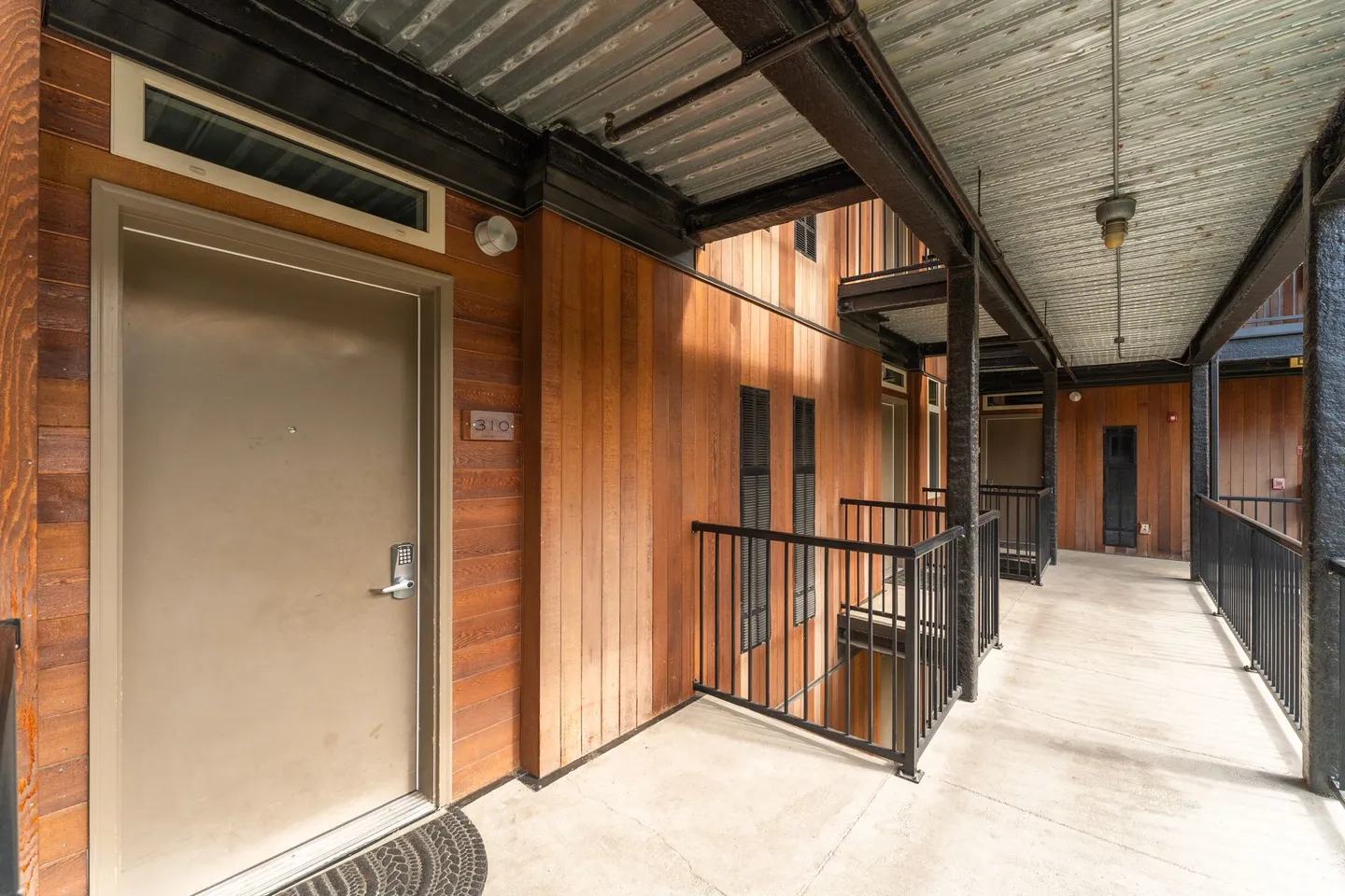 Exterior open-air hallway with wood-paneled walls and unit entrance door marked 310.