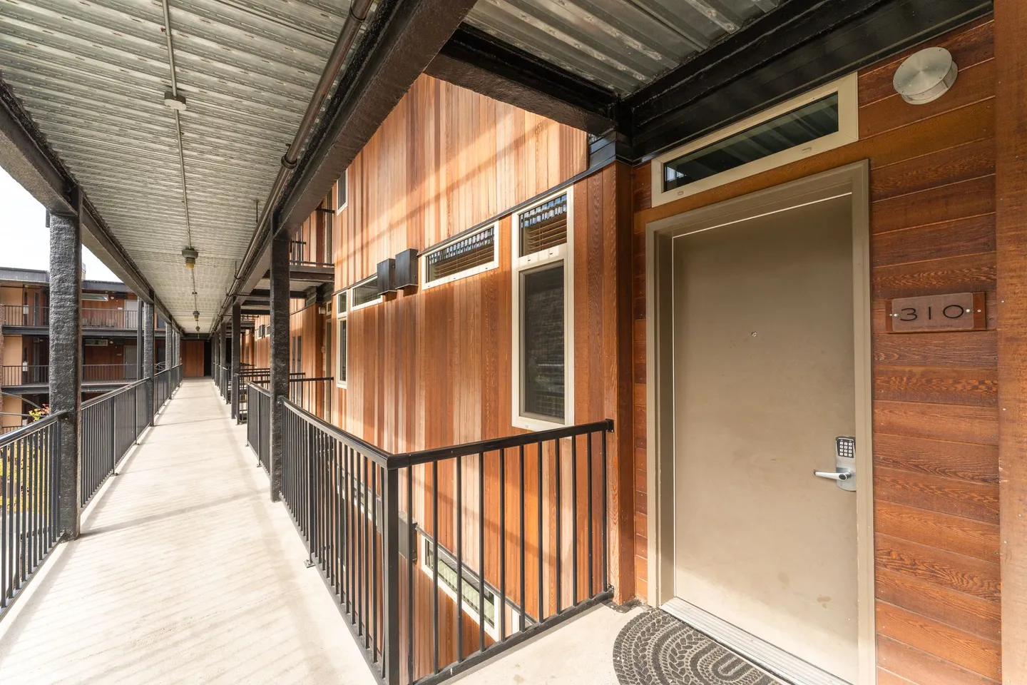 Exterior covered walkway leading to unit 310 featuring wood-paneled walls and black metal railings.