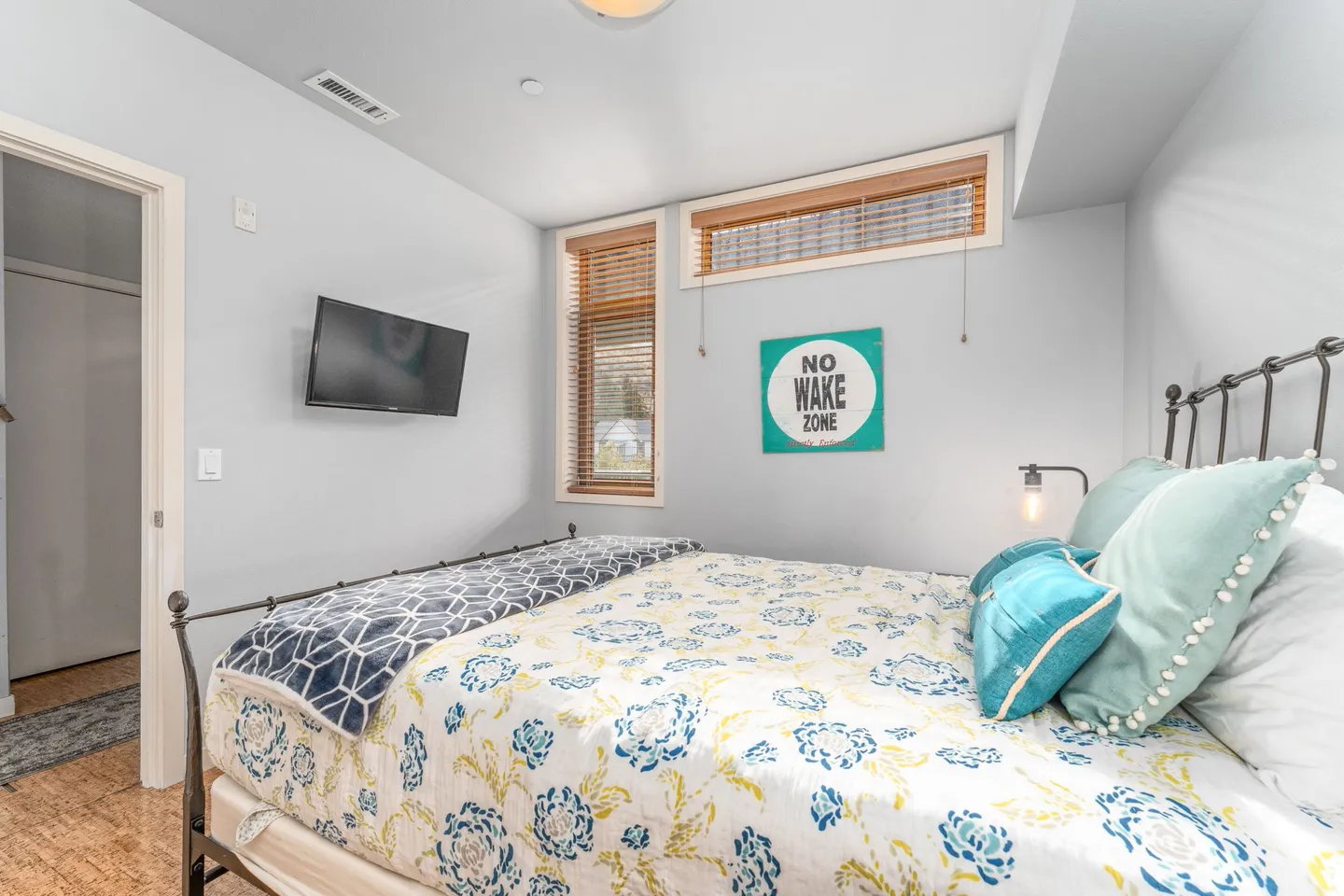 Bedroom with a metal frame bed, floral patterned comforter, wall-mounted television, and high windows.