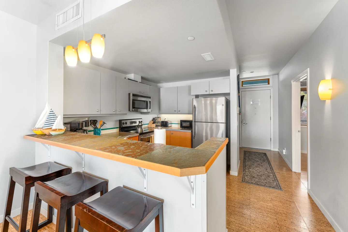 Kitchen with a tiered breakfast bar and barstools looking toward the entry hallway and front door.