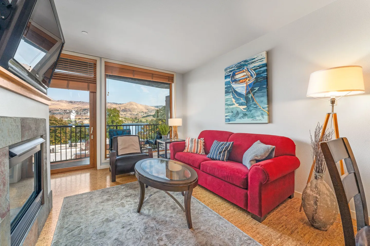 Living room with a red sofa, coffee table, fireplace, and sliding doors opening to a balcony with hillside and water views.