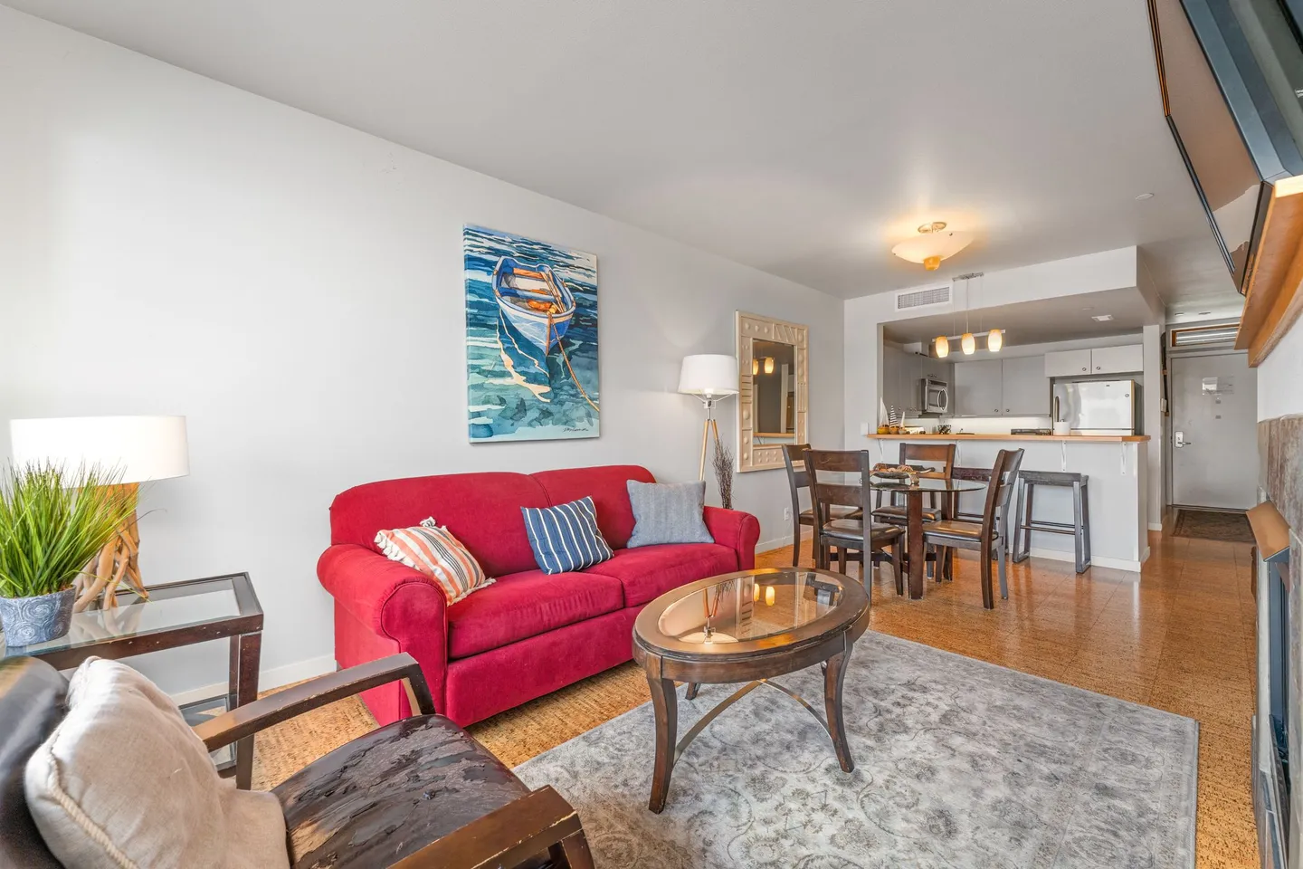 Open-concept living room featuring a bright red sofa, glass-top coffee table, dining set, and view into the kitchen.
