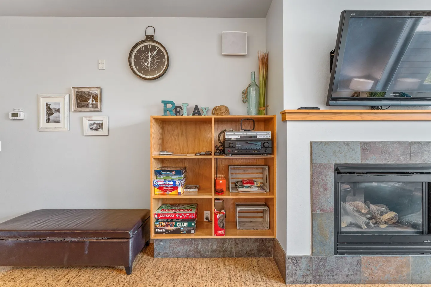 Living room nook with a gas fireplace, a wooden bookcase holding board games and a stereo, and an ottoman next to the wall.