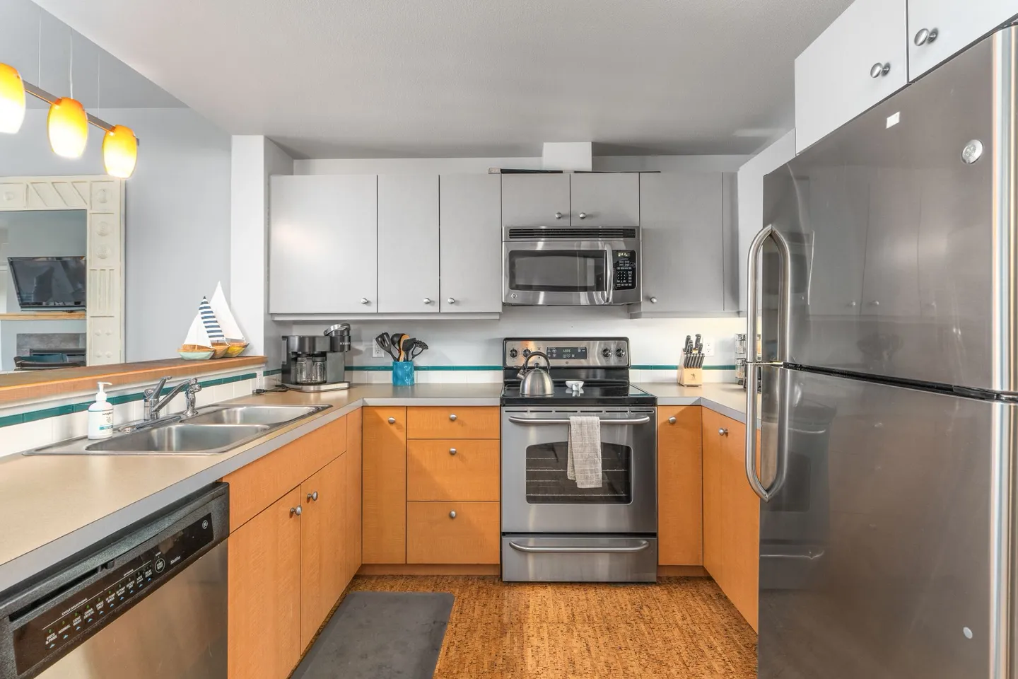 A kitchen with light wood lower cabinets, light gray upper cabinets, and stainless steel appliances including a refrigerator, stove, microwave, and dishwasher.