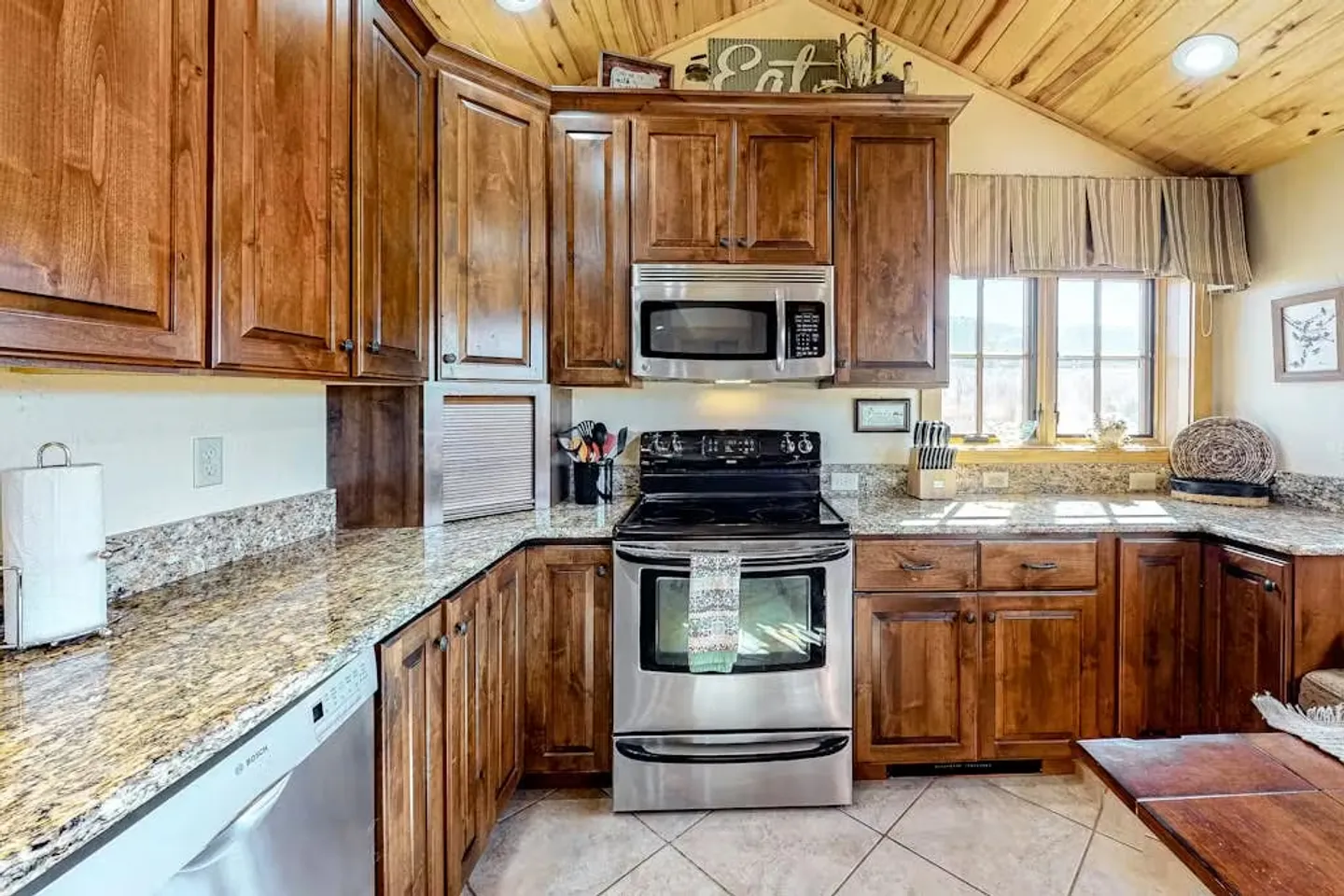 Kitchen corner featuring rich wood cabinetry, speckled granite countertops, and stainless steel appliances beneath a wood-paneled ceiling.