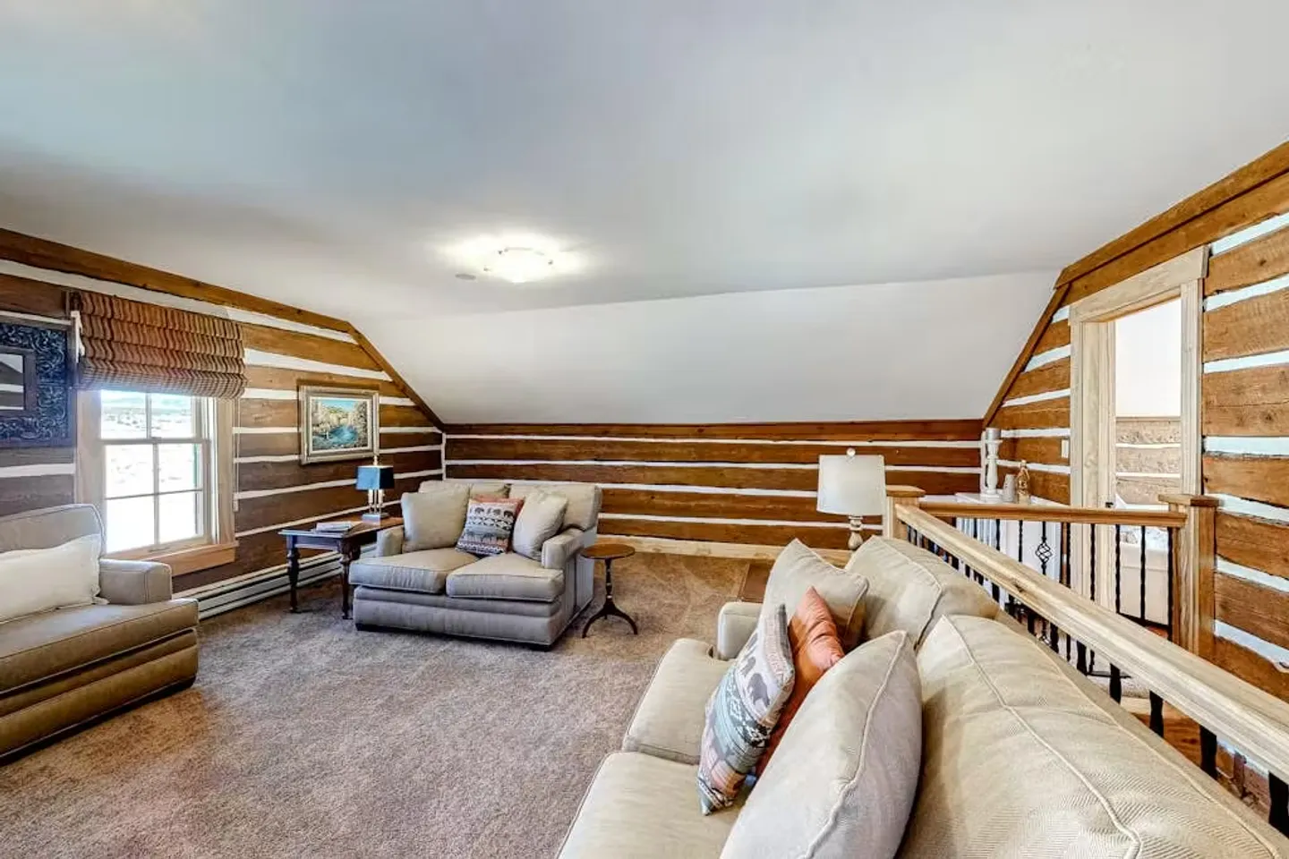 Upstairs loft sitting area with log walls, carpeted floors, and plush armchairs and sofa.