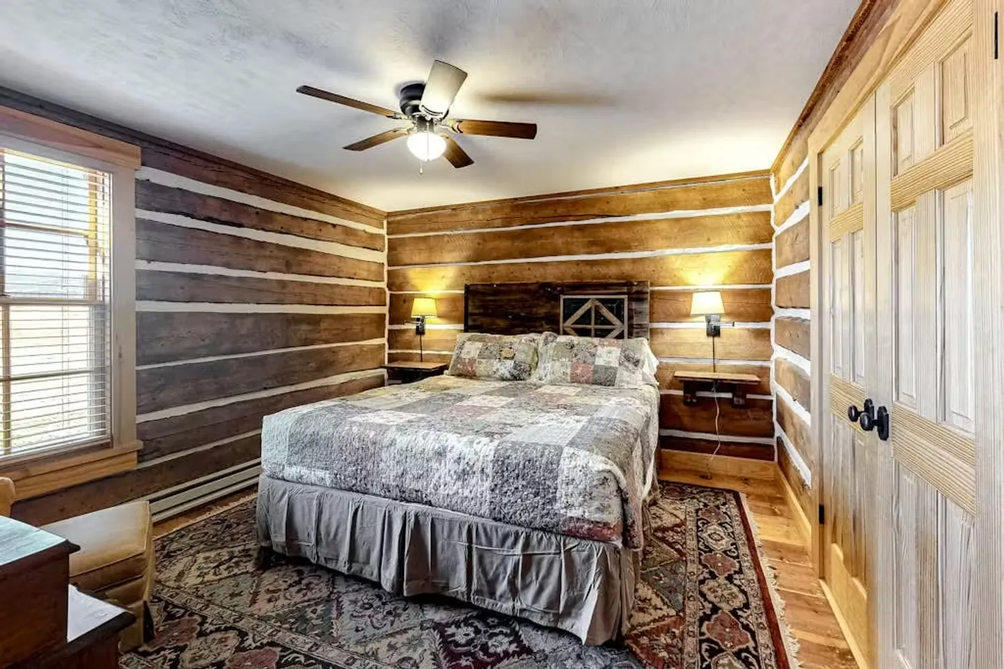 Bedroom with log cabin chinking walls, a bed with a patchwork quilt, an overhead ceiling fan, and wooden doors.