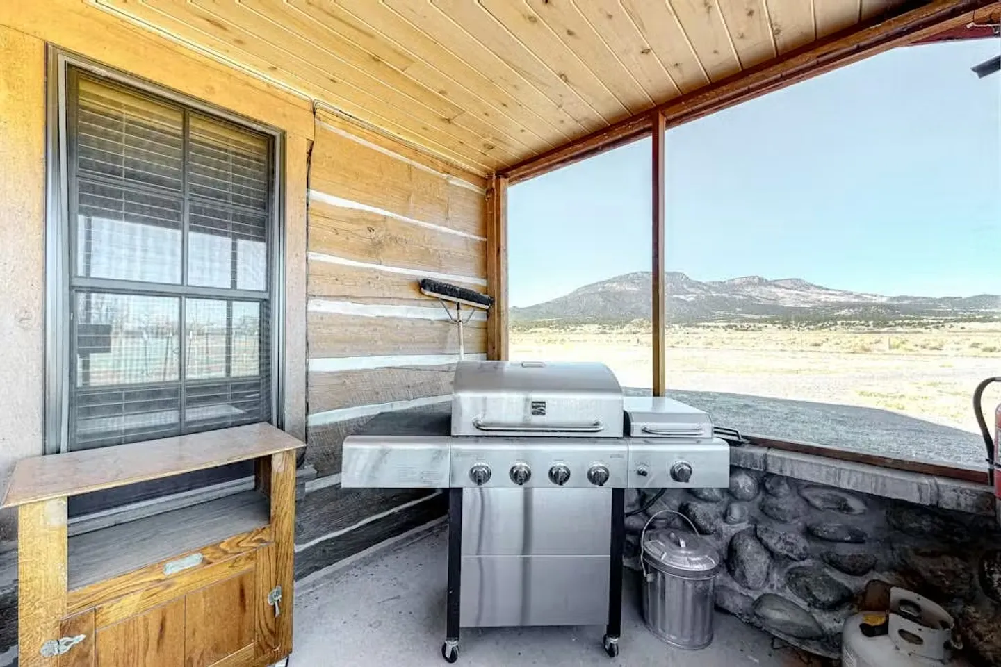 Covered outdoor porch with a stainless steel barbecue grill, log siding, and a view of open desert and mountains.