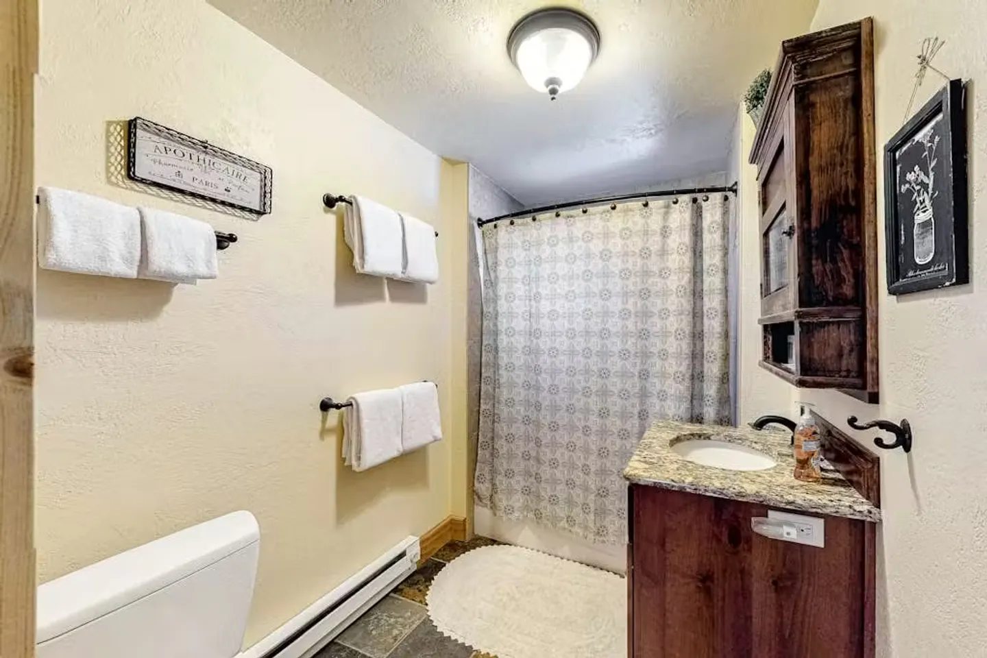 Bathroom featuring a vanity with a stone countertop, a shower-tub combination with a patterned curtain, and multiple wall-mounted towel racks.