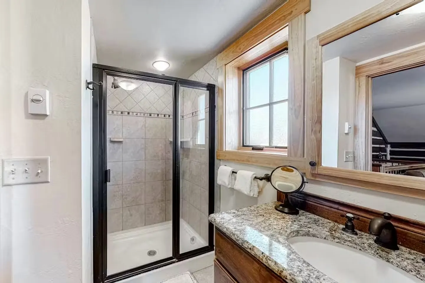 Bathroom with a glass-enclosed walk-in shower and granite countertop vanity next to a window.