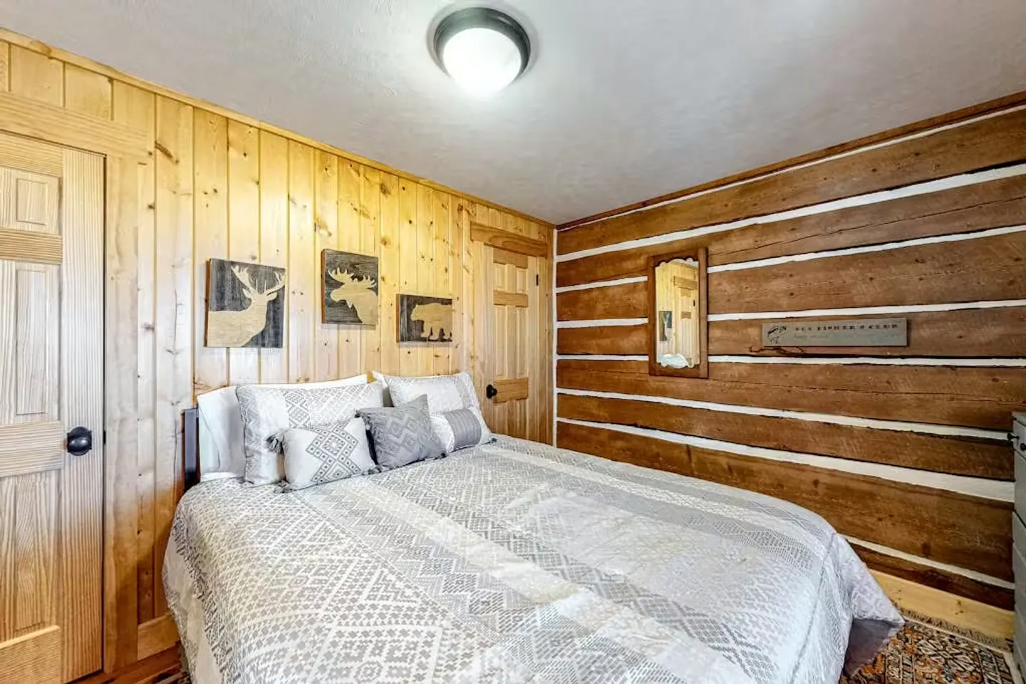 Bedroom with log and wood-paneled walls featuring a made bed with patterned bedding and pillows.