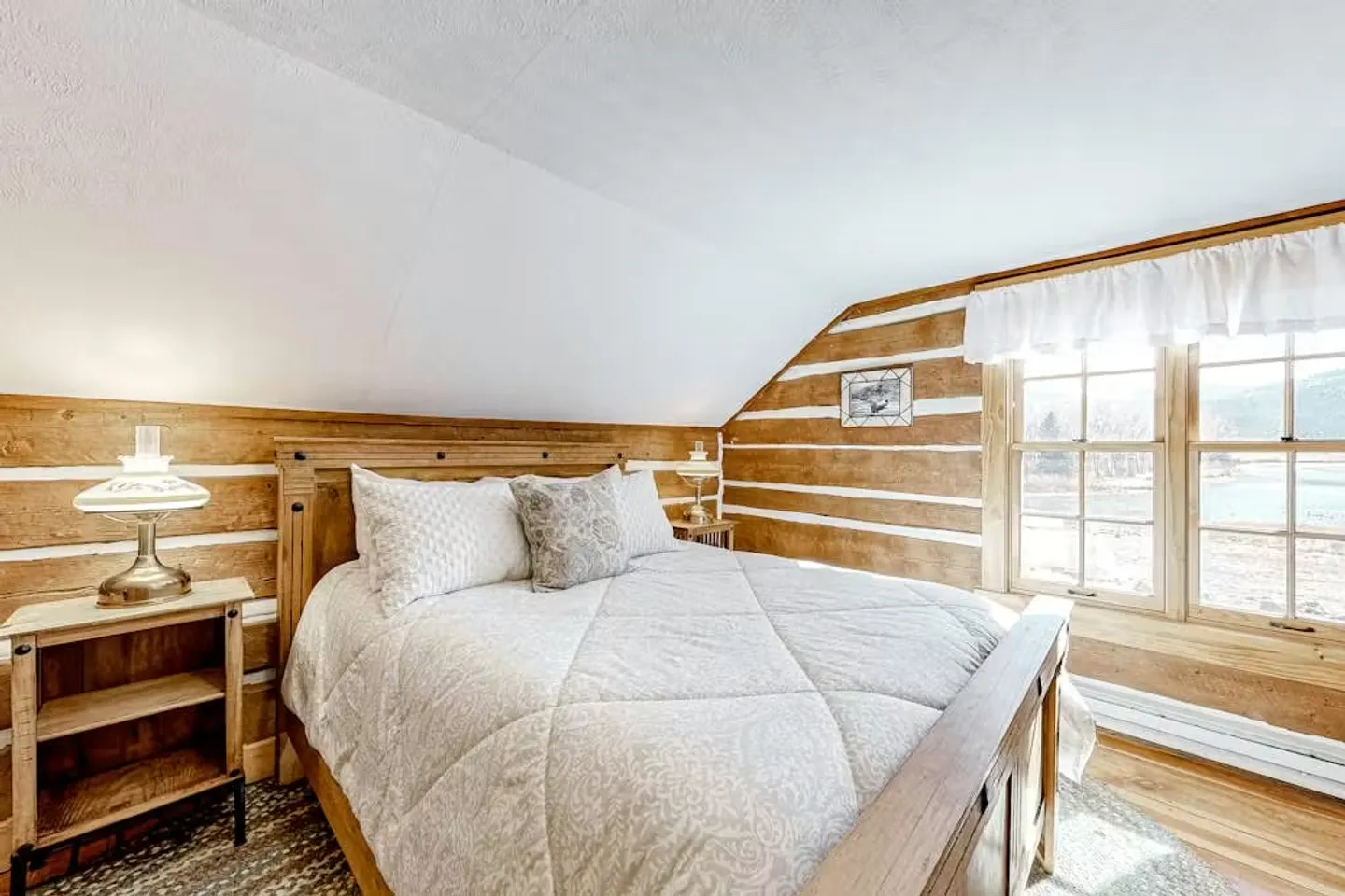 Bedroom with log cabin style walls, a sloped ceiling, a wooden bed, and double windows.