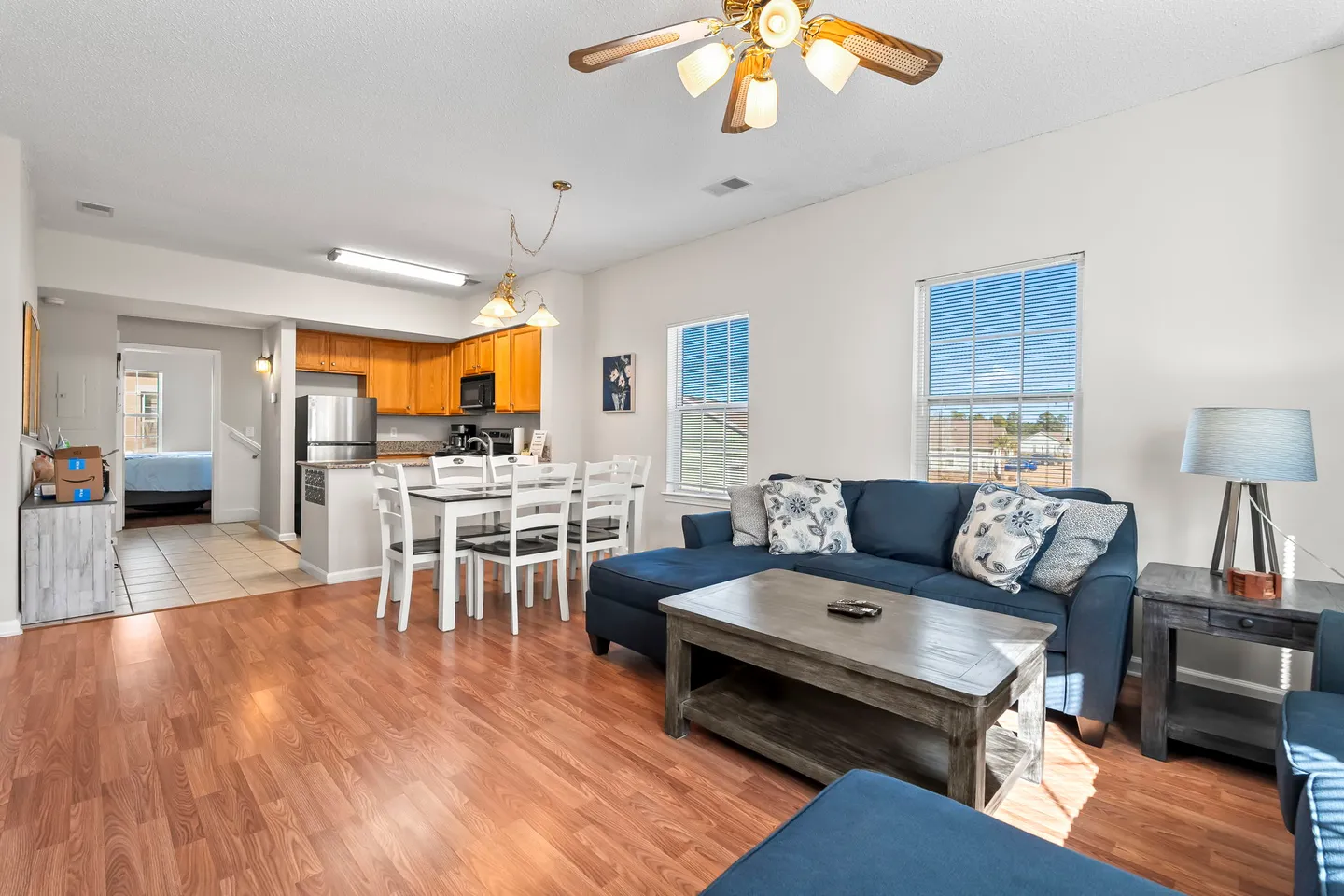 Open concept living room with blue sectional couch, coffee table, dining table, and kitchen in the background.