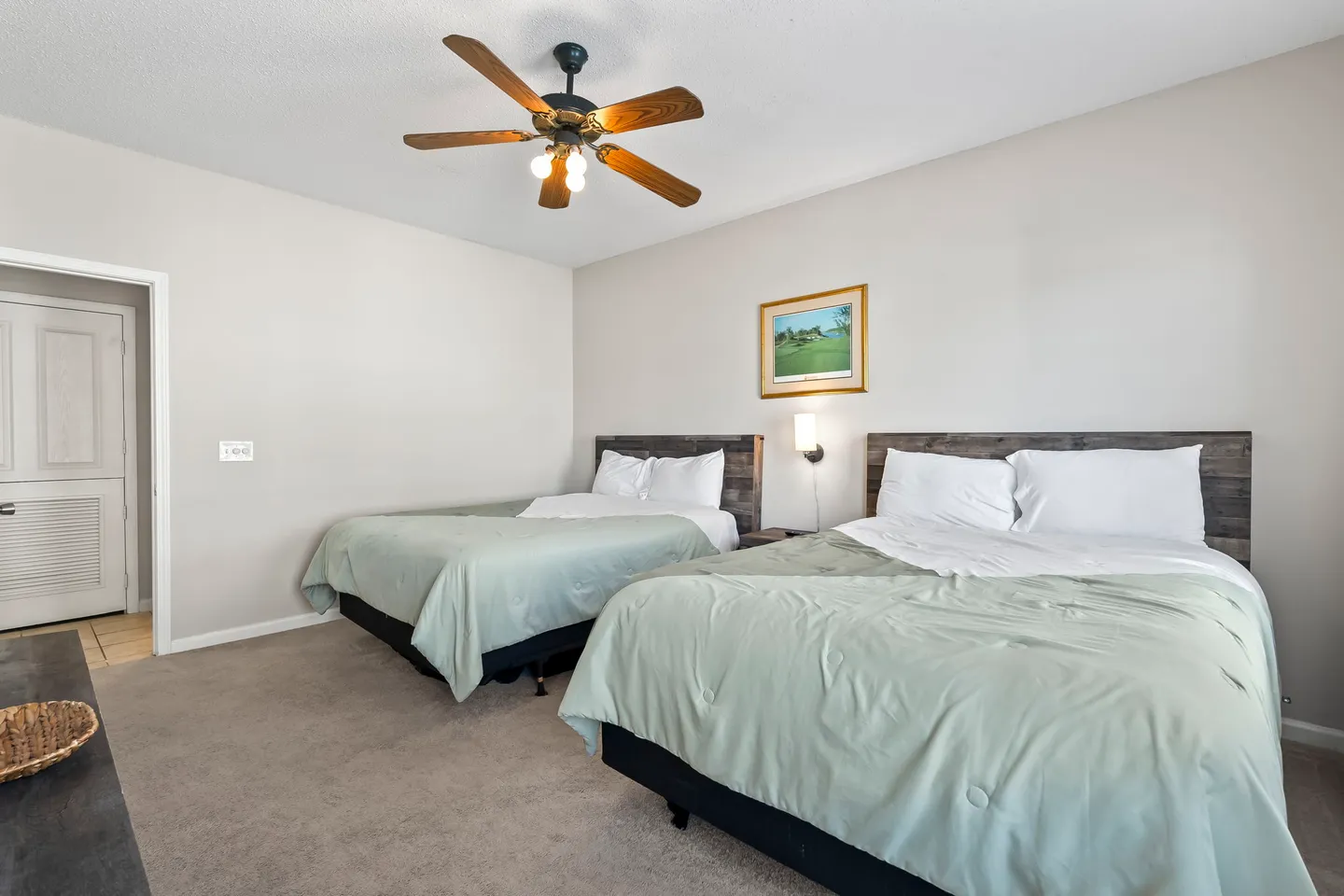 Bedroom featuring two beds with light green bedding, rustic wood headboards, and a ceiling fan with lights.