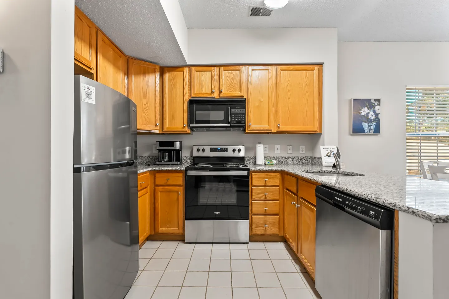 Kitchen with oak cabinets, speckled countertops, stainless steel appliances, and tiled floor.