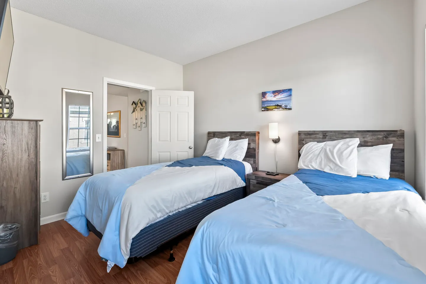 Bedroom with two twin beds dressed in blue and white bedding, wooden headboards, and a doorway leading to an adjoining room.