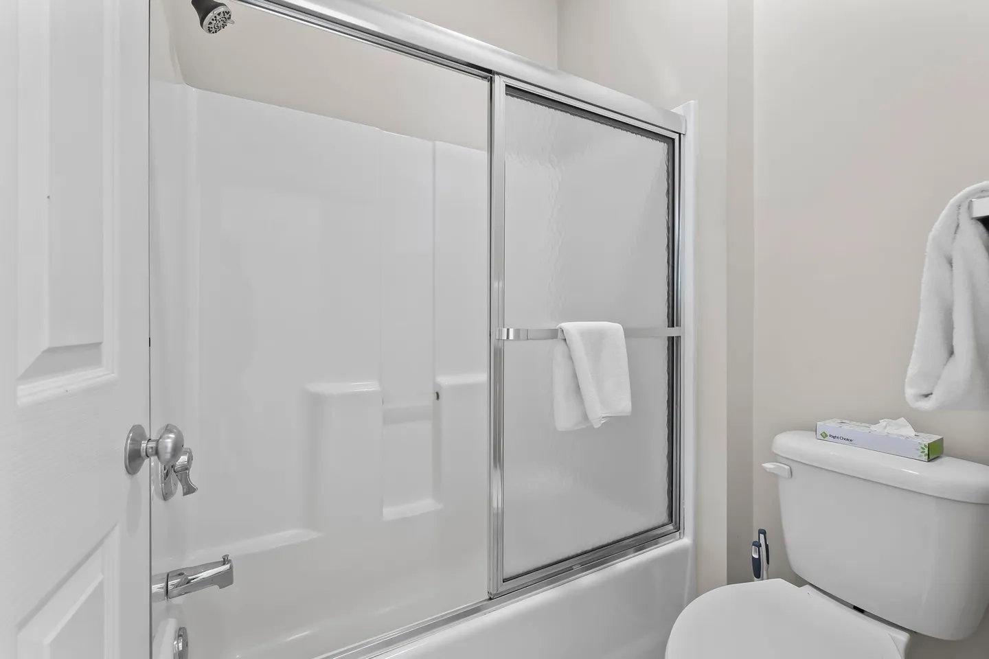 Bathroom showing a white shower and tub combination with sliding textured glass doors and an adjacent toilet.