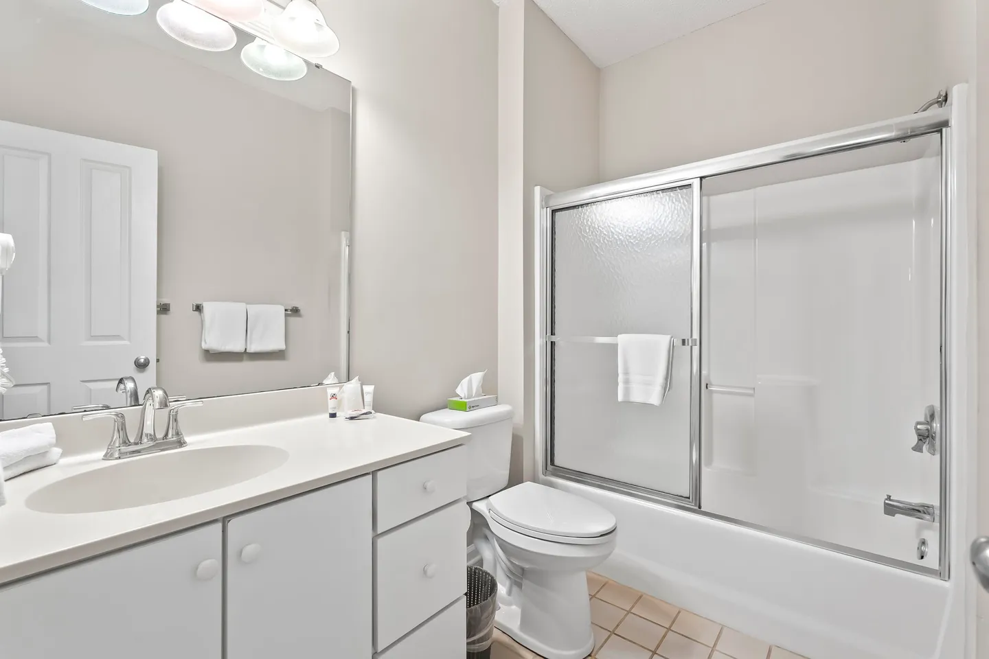 Bathroom with a white vanity, toilet, and a bathtub with sliding glass doors.