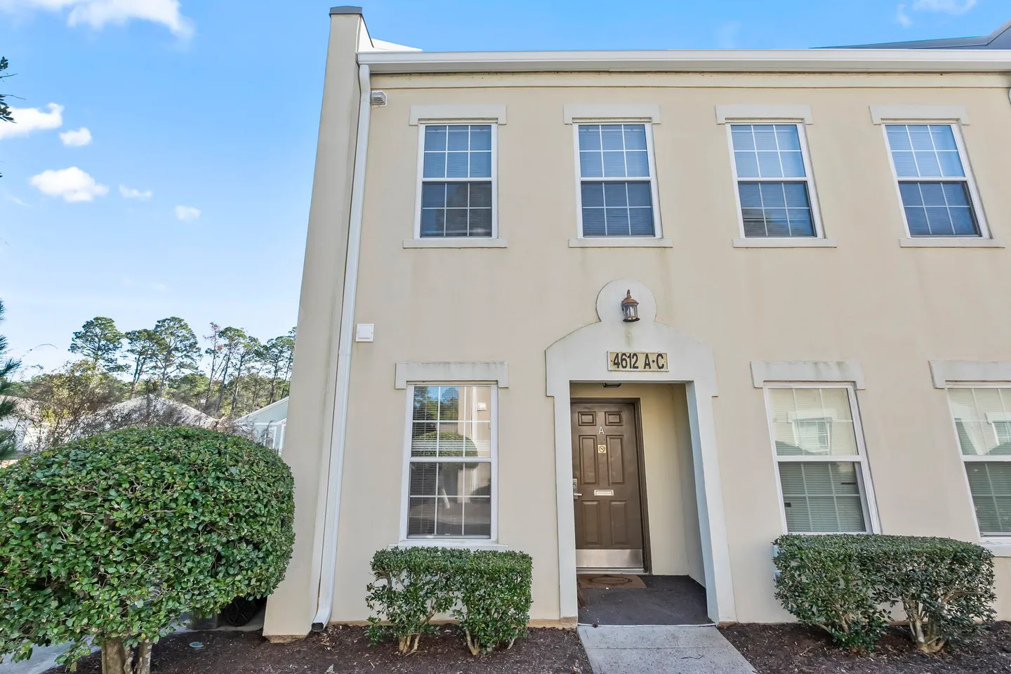 Exterior front entrance and facade of a light-colored townhouse with multiple sash windows and manicured bushes.