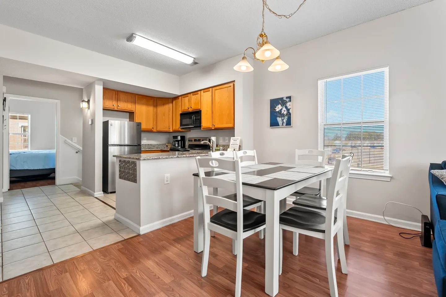 Dining area with a white wooden table and chairs, adjacent to an open kitchen with wooden cabinets and stainless steel appliances.