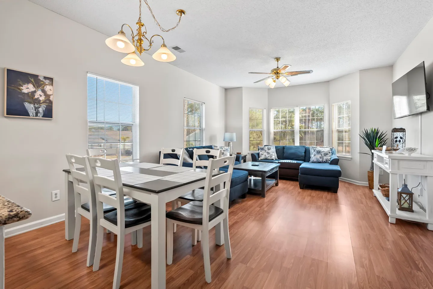 Open-concept living and dining area with wood-look flooring, a dining table with white chairs, and a blue sectional sofa.