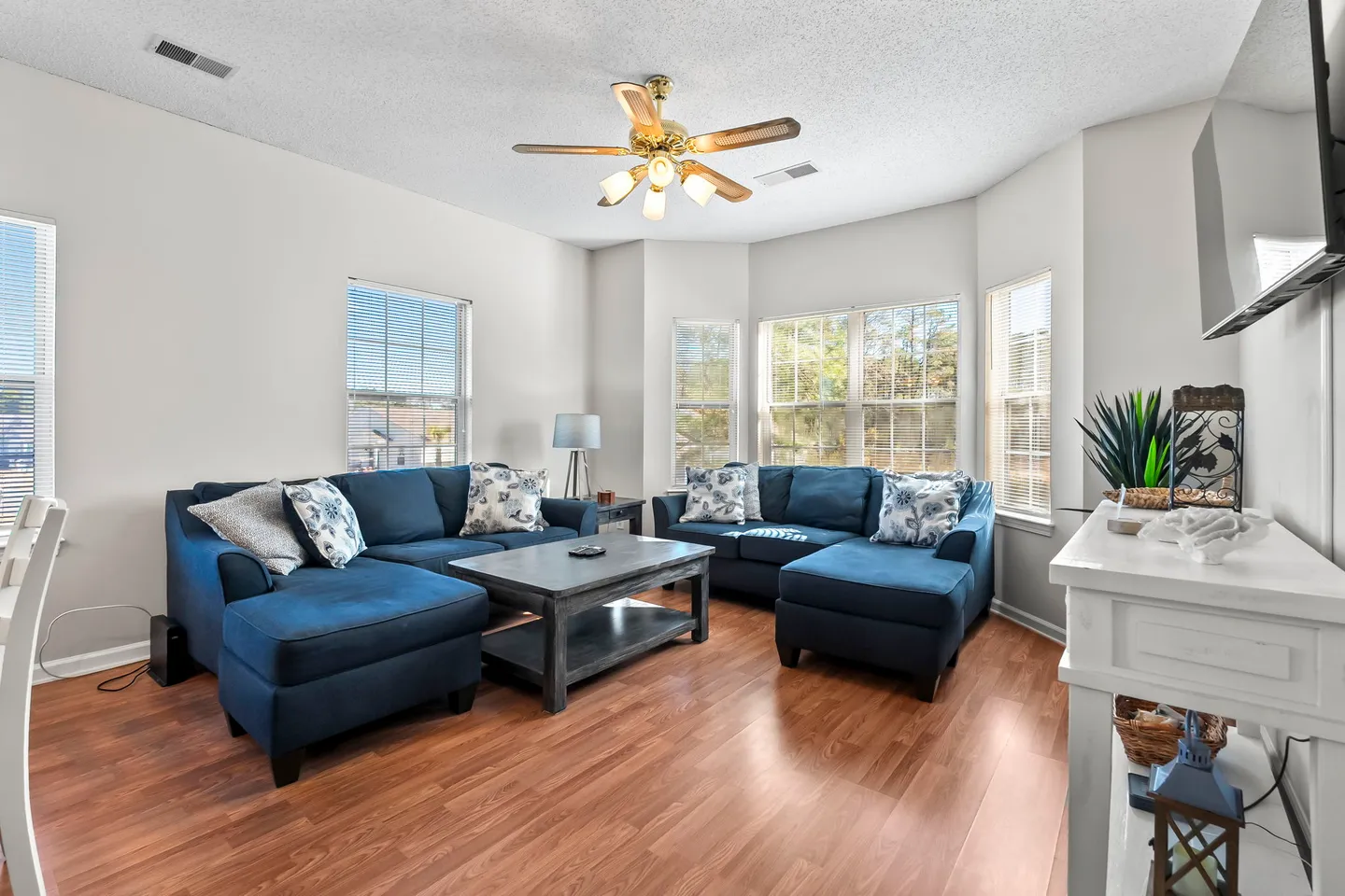 Living room with blue sectional sofas, a central coffee table, wood-style flooring, and a ceiling fan.