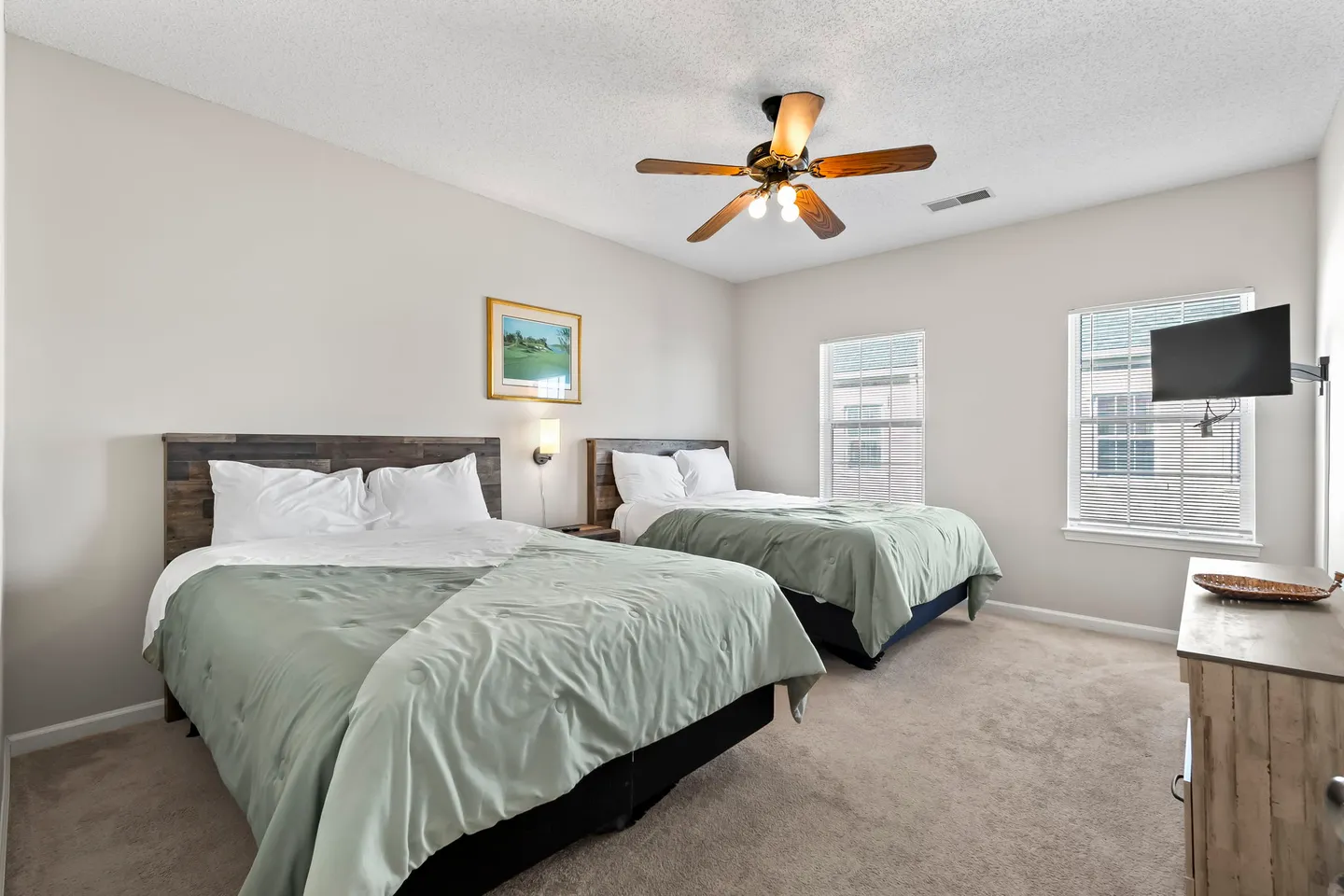 Bedroom with two beds, wood headboards, carpeted floor, ceiling fan, and two windows.