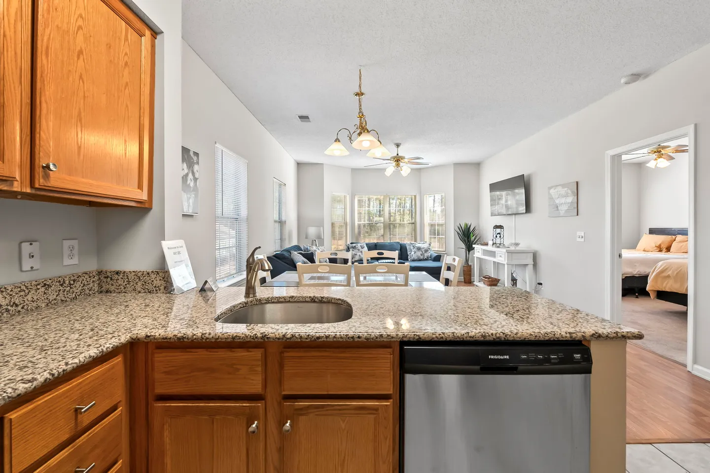 View from kitchen counter showing sink and dishwasher looking into the dining area and living room with a bedroom visible on the right.