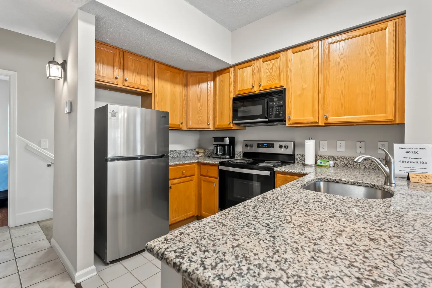 Kitchen with oak cabinets, speckled granite countertops, stainless steel refrigerator, microwave, and electric range.