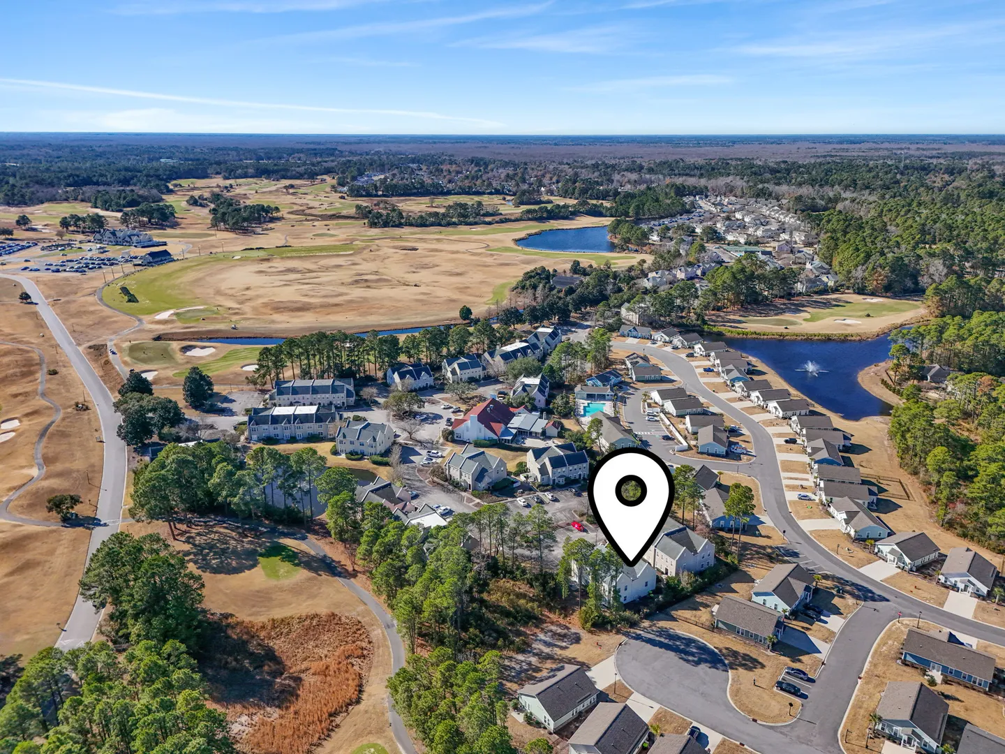 Aerial view of a residential community situated beside golf courses and ponds, with a location pin marking a specific home.