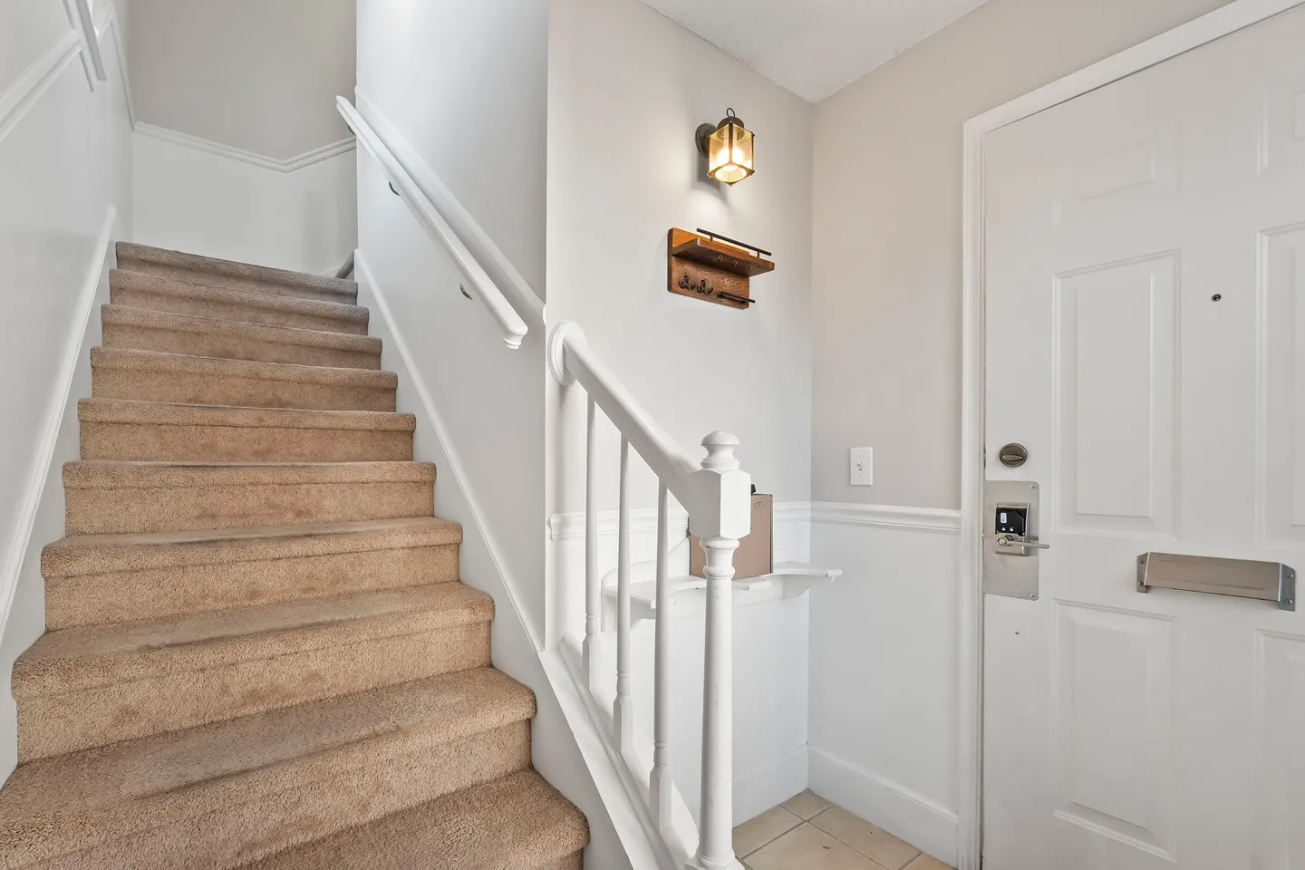 Entryway featuring a front door with an electronic lock next to carpeted stairs with a white railing.