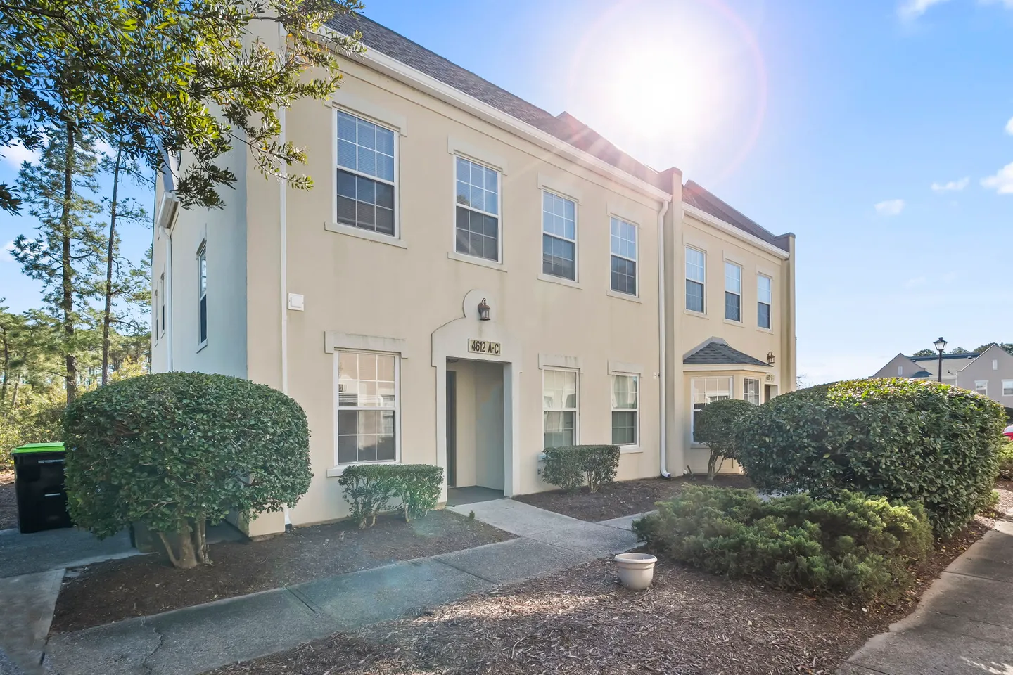 Exterior view of a two-story beige townhouse building on a sunny day with landscaping along the walkway.