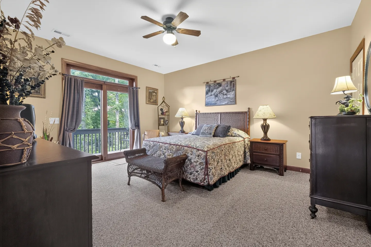 Bedroom with carpeted flooring, a bed with woven headboard, nightstands with lamps, a dresser, and sliding glass doors to a balcony.