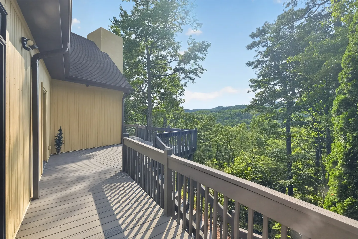 Elevated wooden deck overlooking lush green trees and rolling distant hills on a sunny day.