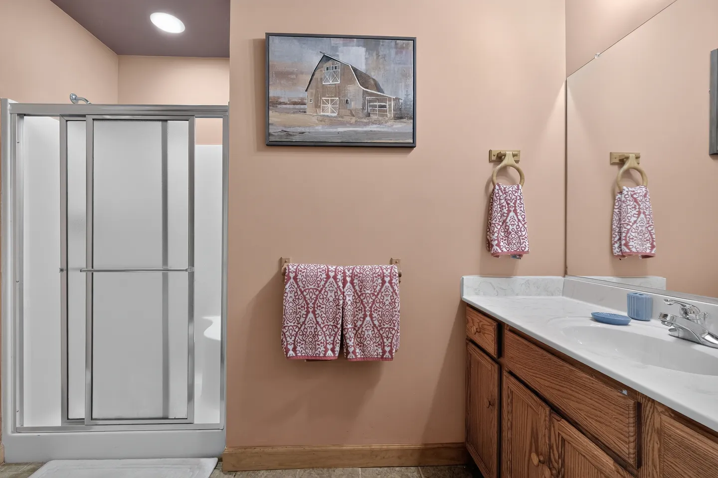 Bathroom featuring a walk-in shower with sliding glass doors, a wood vanity with a white countertop, and peach-colored walls.